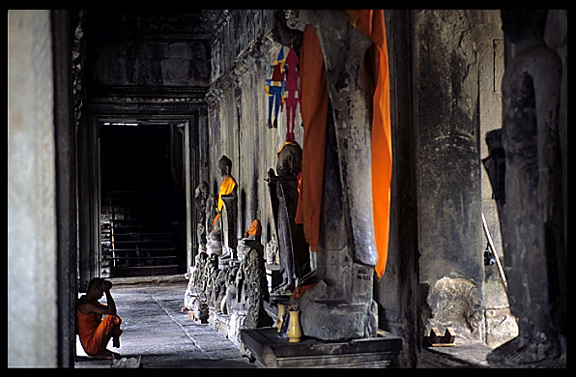 A resting monk in front of Buddha statues inside Angkor Wat.
