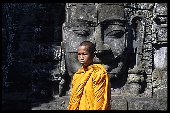 A monk walks in front of one of the Bayon's many faces.