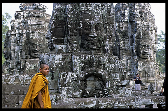 A monk walks in front of one of the Bayon's many faces.