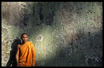 A monk is resting against a weather beaten wall inside Ta Phrom. Siem Riep, Angkor, Cambodia