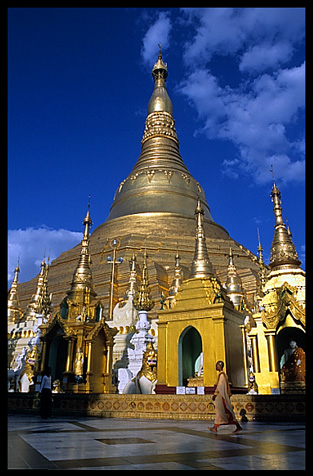 A buddhist nun walking in front of the great golden dome of Shwedagon Paya in Yangon.