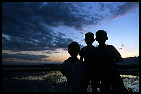 The silhouettes of three Burmese brothers looking into the camera at sunset on Inle Lake.