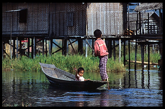 Two Intha children practicing rowing on sampan canoe on Inle Lake.