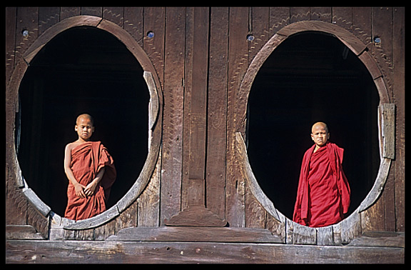 Young monks standing in oval windows of an 18th-century wooden monastery, Shwe Yaunghwe Kyaung.