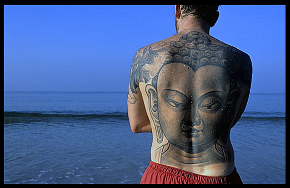 A tourist with an image of Buddha tattooed on his back, looking out over the sea.