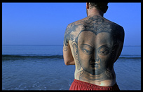 A tourist with an image of Buddha tattooed on his back, looking out over the sea.