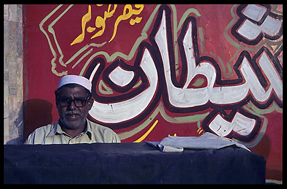 Portrait of a Pakstani in front of a hand painted advertisement. Peshawar, Pakistan