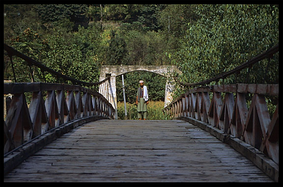 A Pashtun crosses the Swat river on one of the many bridges . Madyan, Pakistan