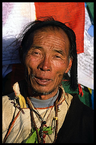Old tibetan pilgrim in front of prayer flags.