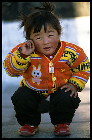 A girl with a Buddha amulet playing on the Jokhang square.