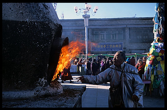 A pilgrim is lightening the stone sangkang (incense burner) in front of the Jokhang.