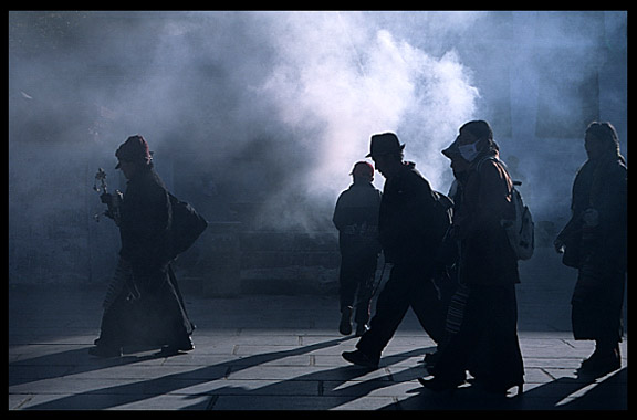 Smoke from the incense burners creates silhouettes of passing by pilgrims.