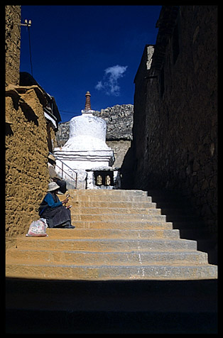 A pilgrim is resting on the stairs of Drepung Monastery.