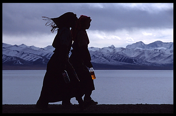 The silhouettes of two pilgrims with the snowy Nyenchen Tanglha massif (7111m) in the background.