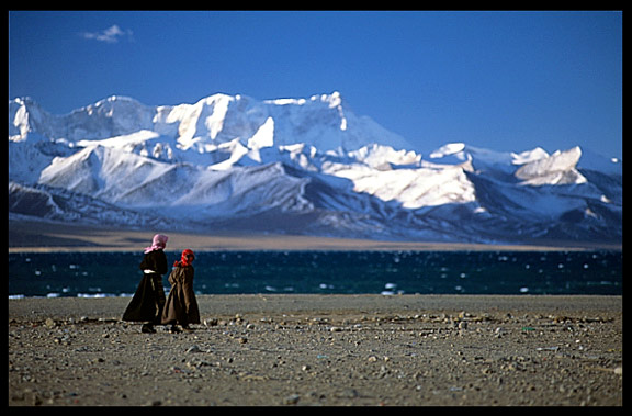 Pilgrims walking the Nam Tso Kora with clear turquoise water and the magnificent snowy Nyenchen Tanglha massif (7111m) on the background.